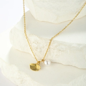Elegant gold ginkgo leaf and pearl pendant necklace displayed on a white textured stone