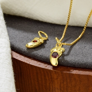 Detailaufnahme von Baby-Fuß-Anhänger aus Gold mit rotem Zirkon auf grauem Samt