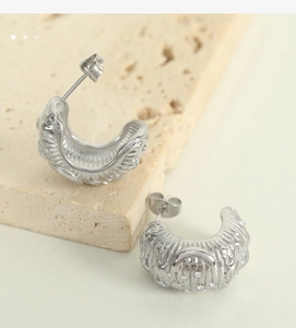 Macro shot of silver C-shape hoop earrings with wave texture and sparkling zircons