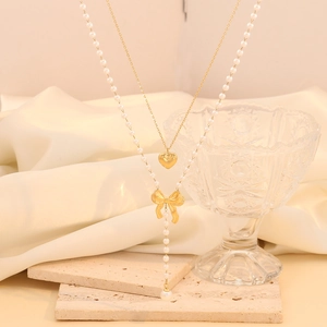 Double-layered gold necklace with heart and bow pendants and faux pearl tassel detailing