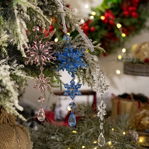 Pink blue and clear acrylic snowflake ornaments hanging on a snowy Christmas tree branch