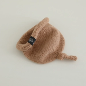 Détail du bonnet de bébé en tricot camel doux avec nœud supérieur et écusson noir