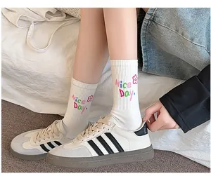 Detail of white crew socks with Nice Day embroidery and floral patterns worn with sneakers