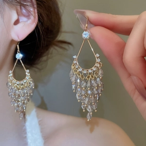 Detail of drop-shaped gold earrings with sparkling crystals and grey-purple tassels