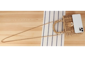 Detail view of woven straw handbag featuring a gold metal lock and chain strap