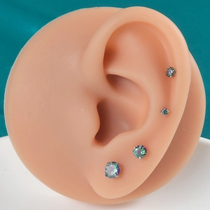 Macro view of 4-prong iridescent opal cartilage earrings on a silicone ear model