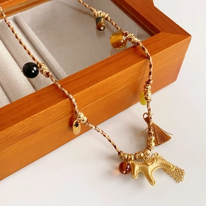 Detail of a brown woven necklace with a golden pony charm and beads on a jewelry box