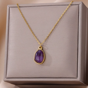 Macro detail of purple gemstone pendant on gold chain resting on a jewelry box edge