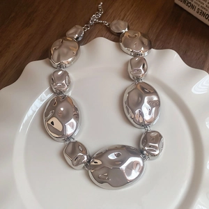 Polished silver oval link necklace displayed on white ceramic plate on wooden desk