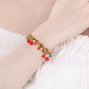 Close-up of summer fruit charms on a gold chain bracelet worn on a female wrist