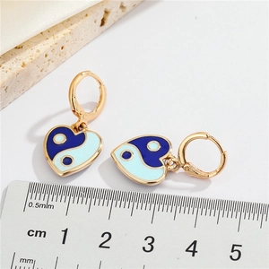 Golden heart earrings with blue yin-yang enamel design displayed on a white stone base