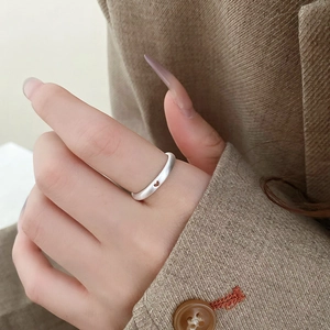 Close-up of a silver ring with heart cut-out design on a hand over beige fabric