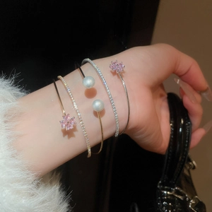 Detail of layered gold bracelets with pink crystal flowers and pearls on model