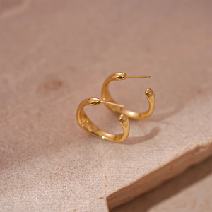 Détail macro de boucles d'oreilles créoles dorées en U sur fond de pierre naturelle