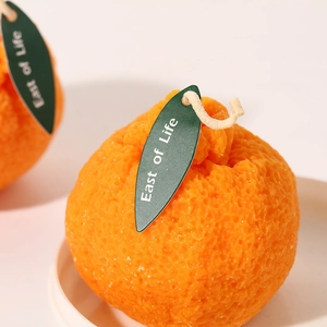 Vela aromática realista con forma de naranja, cáscara texturizada y detalle de hoja