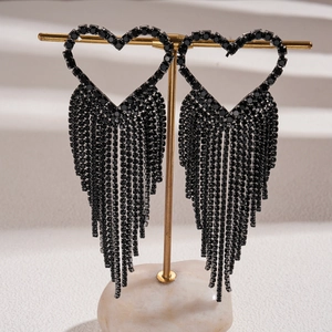 Detail view of heart-shaped black rhinestone tassel earrings on a gold stand