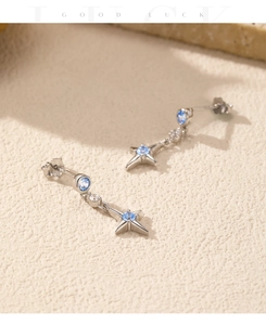 Détail des boucles d'oreilles étoile en argent avec une pierre bleue sur fond de pierre