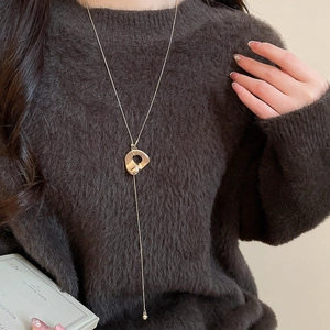 Detail einer goldenen Halskette mit unregelmäßigem Anhänger und Quasten auf einem Pullover