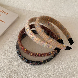 Detail of four colorful knit tweed headbands in beige, brown, and black stacked on a table