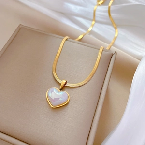 Detailed macro view of gold heart pendant with iridescent shell on snake chain