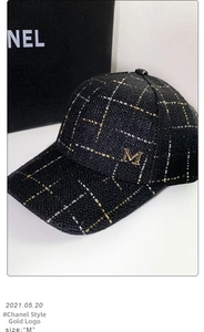 Detail of black tweed baseball cap with gold metallic M logo and woven texture