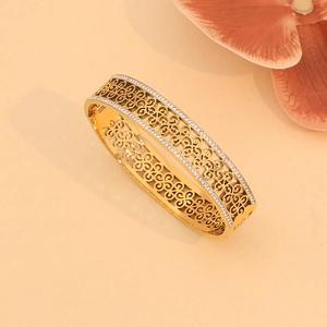 Golden wide bangle featuring hollow flower patterns and rhinestones on a beige surface