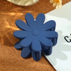 Nahaufnahme einer matt dunkelblauen Blumen-Haarklammer im Gänseblümchen-Design auf Kork