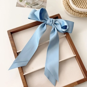 Detail of light blue satin bow hair clip on a wooden tray with a minimalist aesthetic