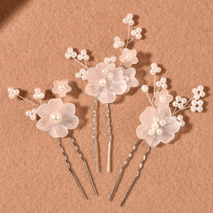 Detailed shot of three bridal hair pins with frosted white flowers and pearls on brown fabric
