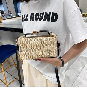 Detail of beige woven straw handbag with black leather straps and golden metal lock buckle