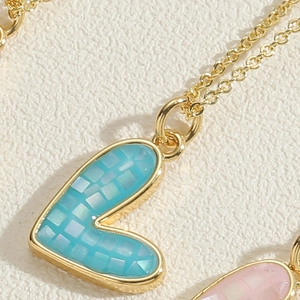 Macro detail of gold heart pendant with blue mosaic shell inlay and fine chain