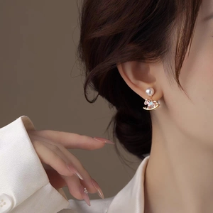 Close-up of elegant gold rocking horse pearl earrings with pink enamel on a female model