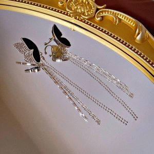Detail of silver butterfly ear clip with rhinestones and long fringe tassels on mirror