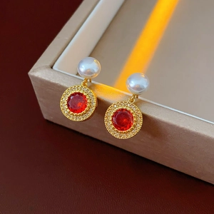 Détail de boucle d'oreille dorée avec pierre rouge et perle sur une boîte à bijoux
