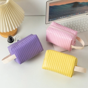 Tre borse da trucco in pelle PU trapuntata in viola, rosa e giallo su una scrivania