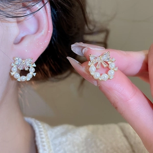 Macro detail of elegant pearl stud earrings with sparkling crystal bow on a golden wreath