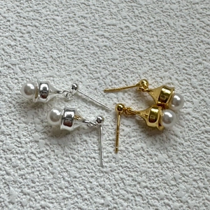 Detailed view of silver and gold bell-shaped pearl earrings on a textured background
