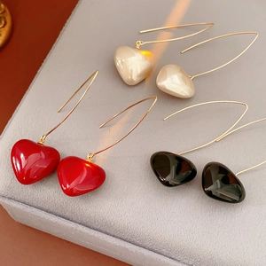 Close-up of heart-shaped drop earrings in red, black and beige on gray velvet