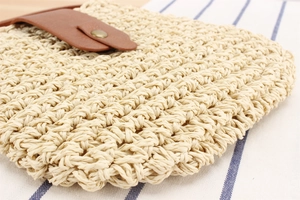 Detail of paper rope woven crossbody bag with brown leather flap and bronze button