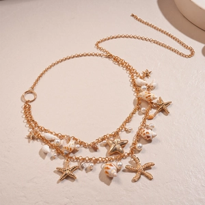 Detail of layered gold starfish and conch body chain with white pearls on beige background
