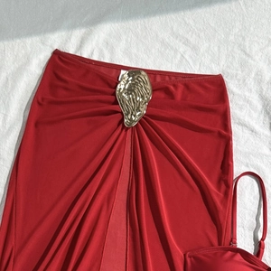 Detailed view of red bikini wrap skirt featuring a central gold irregular metal buckle