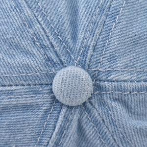 Detail of light blue washed denim baseball cap with white double stitching and top button