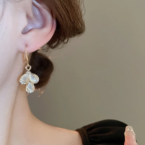 Macro shot of gold teardrop clover earrings with faux cat eye stones and micro pavé