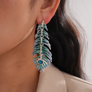 Détail de boucles d'oreilles en plumes avec strass bleus et verts portées par un modèle