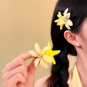 Nahaufnahme von eleganten gelben Stoffblumen- und Seestern-Haarspangen an geflochtenem Haar.