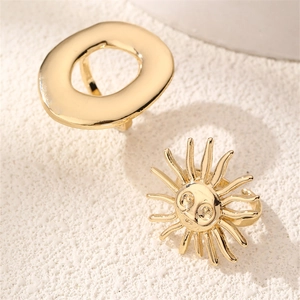 Macro detail of gold sun face and minimalist oval rings on textured stone base