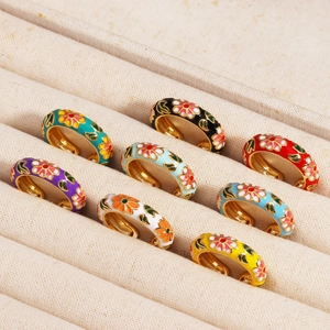 Colorful floral enamel rings in gold finish displayed on a beige jewelry tray