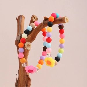 Detail of colorful beaded bracelets with flower charms hanging on a rustic wood branch