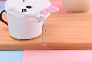 Close-up of white plush cat coin purse with blue embroidered eyes on ceramic cup