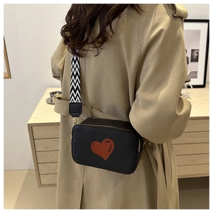 Detail of black rectangular crossbody bag with red heart and patterned wide strap